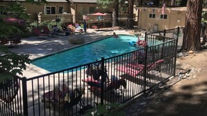 A swimming pool with lounge chairs and a fenced area, surrounded by trees and buildings. - Sugar Pine 3 Bedroom Home by RedAwning (Incline Village)