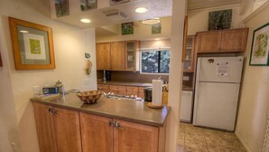 A kitchen with wooden cabinets, a countertop, a sink, a refrigerator, and a window with a view of trees. - Sugar Pine 3 Bedroom Home by RedAwning (Incline Village)