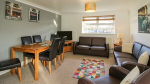 Ein Wohnzimmer mit Esstisch, Stühlen, einer Couch, einem Fernseher und Kunstwerken an den Wänden.