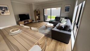 Ein modernes Wohnzimmer mit einem Holzesstisch, einem grauen Sofa und einem Fernseher auf einer Holzkommode.