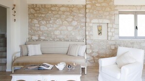 Ein gemütliches Zimmer mit einer Steinwand, einem Sofa, einem Sessel und einem Tisch mit einem Buch und einer Teekanne.