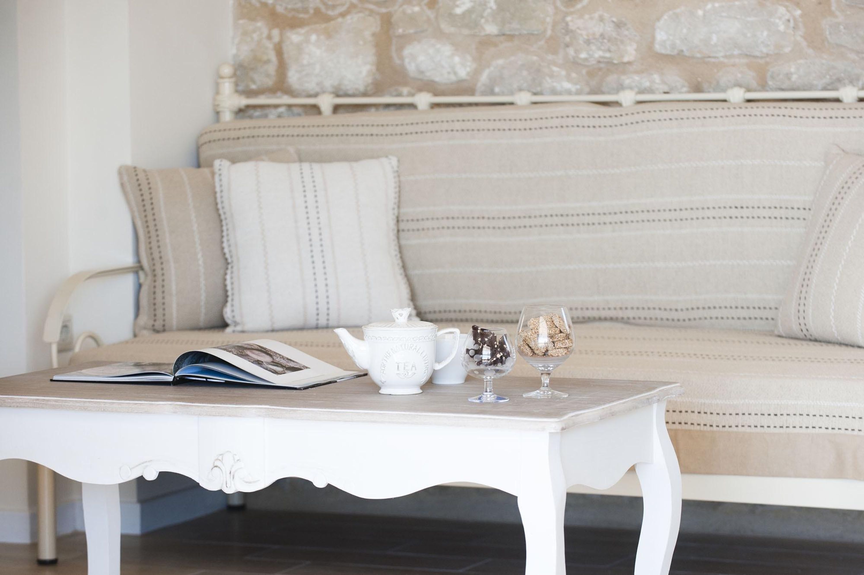 Un canapé blanc avec des coussins à rayures, une table blanche sur laquelle se trouve un livre, une théière et un verre de mousse au chocolat.
