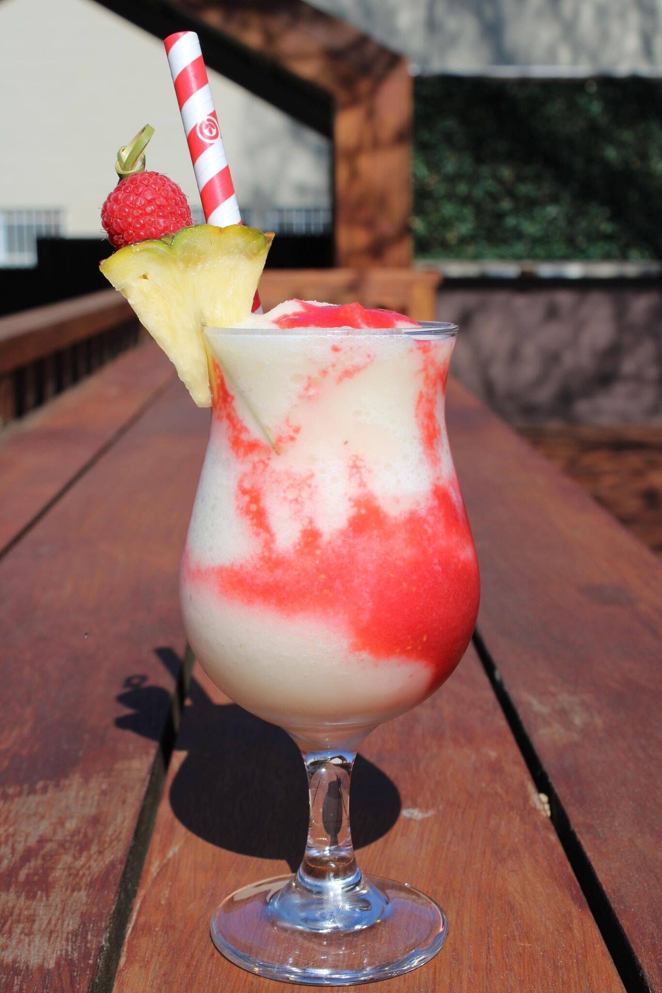 A tropical drink in a glass with a straw, garnished with a strawberry and pineapple slice, on a wooden table.