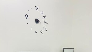 Ein modernes Wohnzimmer mit Flachbildfernseher, Wanduhr, Holzkonsole mit Spiegel und schwarzem Papierkorb.