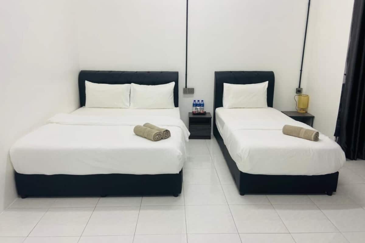 A hotel room with two beds, each with white bedding and dark headboards. There are two bedside tables, one with a lamp and the other with bottled water.