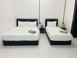 A hotel room with two beds, each with white bedding and dark headboards. There are two bedside tables, one with a lamp and the other with bottled water. - JK Roomstay (Jasin)