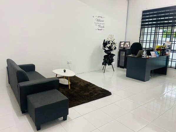 Un espacio de oficina moderno con un conjunto de sofás, una pequeña mesa redonda, un escritorio con una computadora y una planta decorativa.