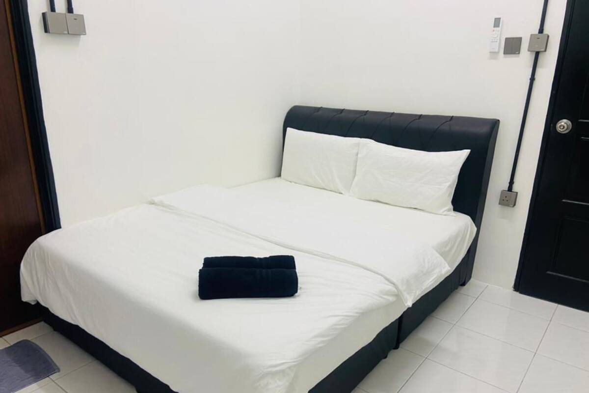 A neatly made bed with white bedding and a dark headboard in a room with white walls and a tiled floor.