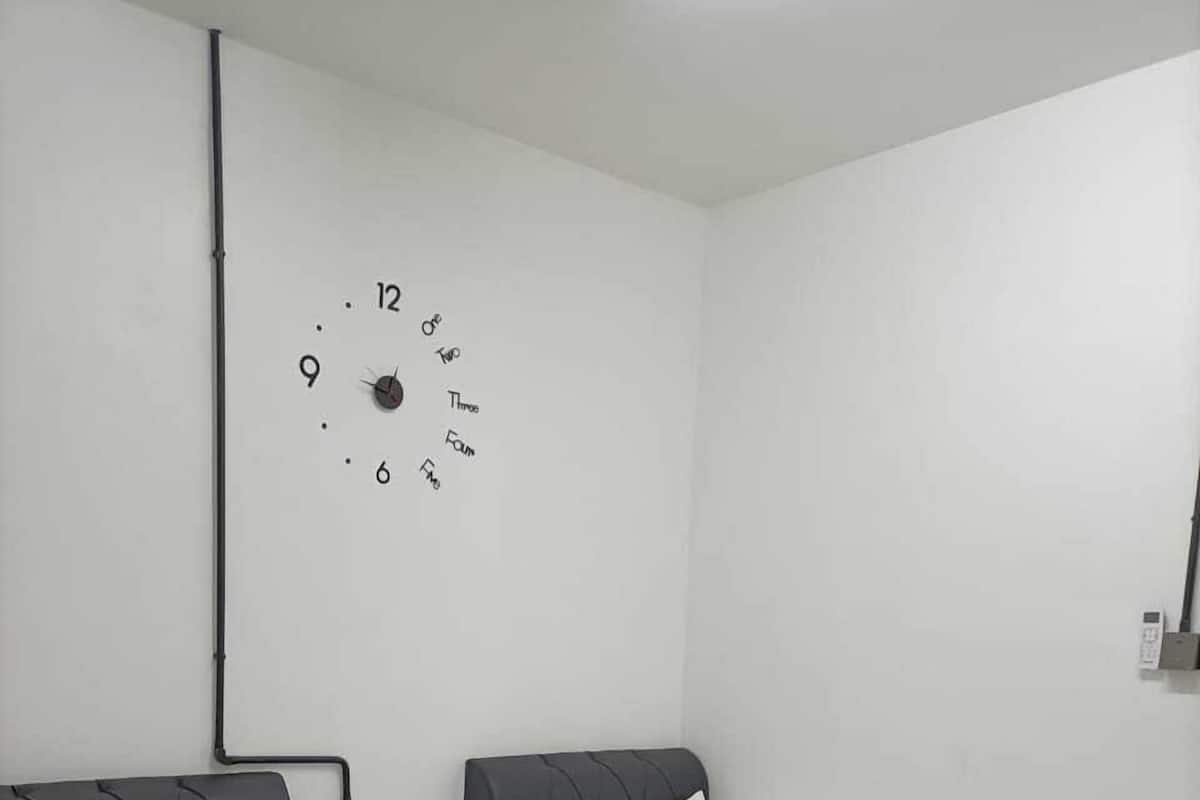 A hotel room with two single beds, a wall clock, a bedside lamp, and a power outlet.