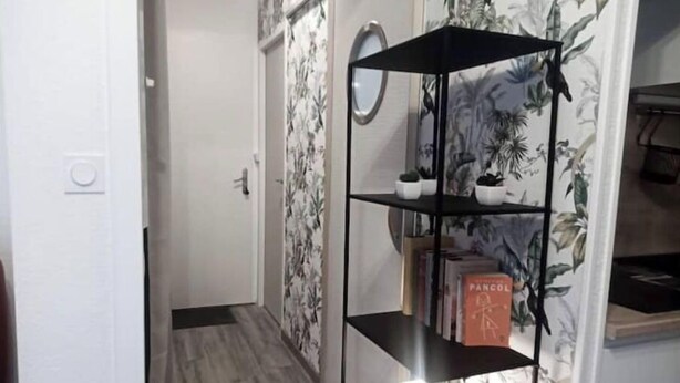A hallway with a black metal shelf unit against a wall with floral wallpaper, a round mirror, and a door at the end. - nice apartment very well located, covered parking (Lourdes)