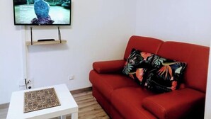 A living room with a red sofa, a television mounted on the wall, and a small white table with a decorative item. - nice apartment very well located, covered parking (Lourdes)