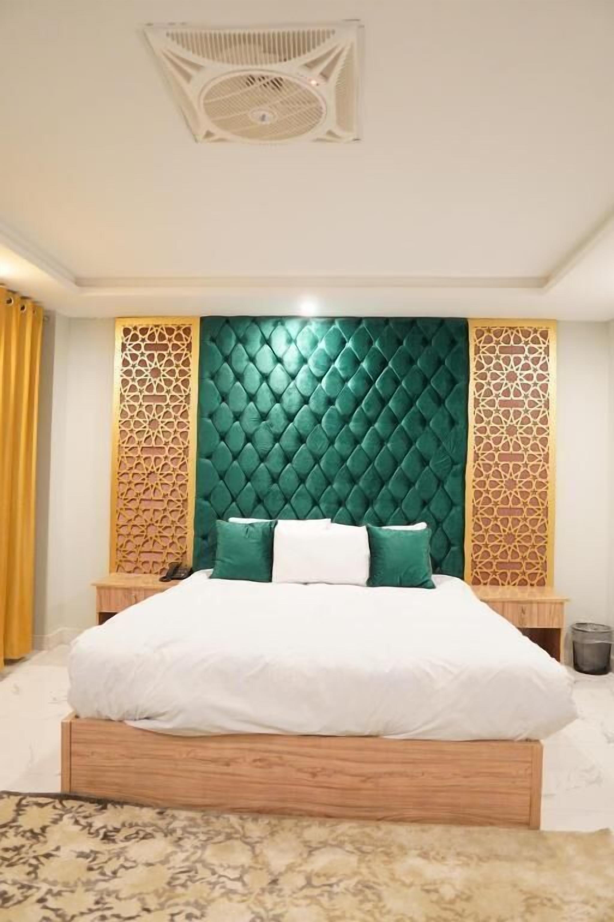 Ein Schlafzimmer mit einem gesteppten, grünen Kopfteil, einem Holzbettgestell und einem gemusterten Teppich.
