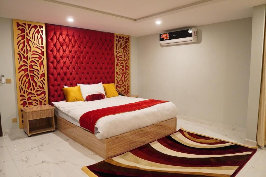 A bedroom with a tufted red headboard, a wooden bed frame, a white mattress, and a striped area rug.