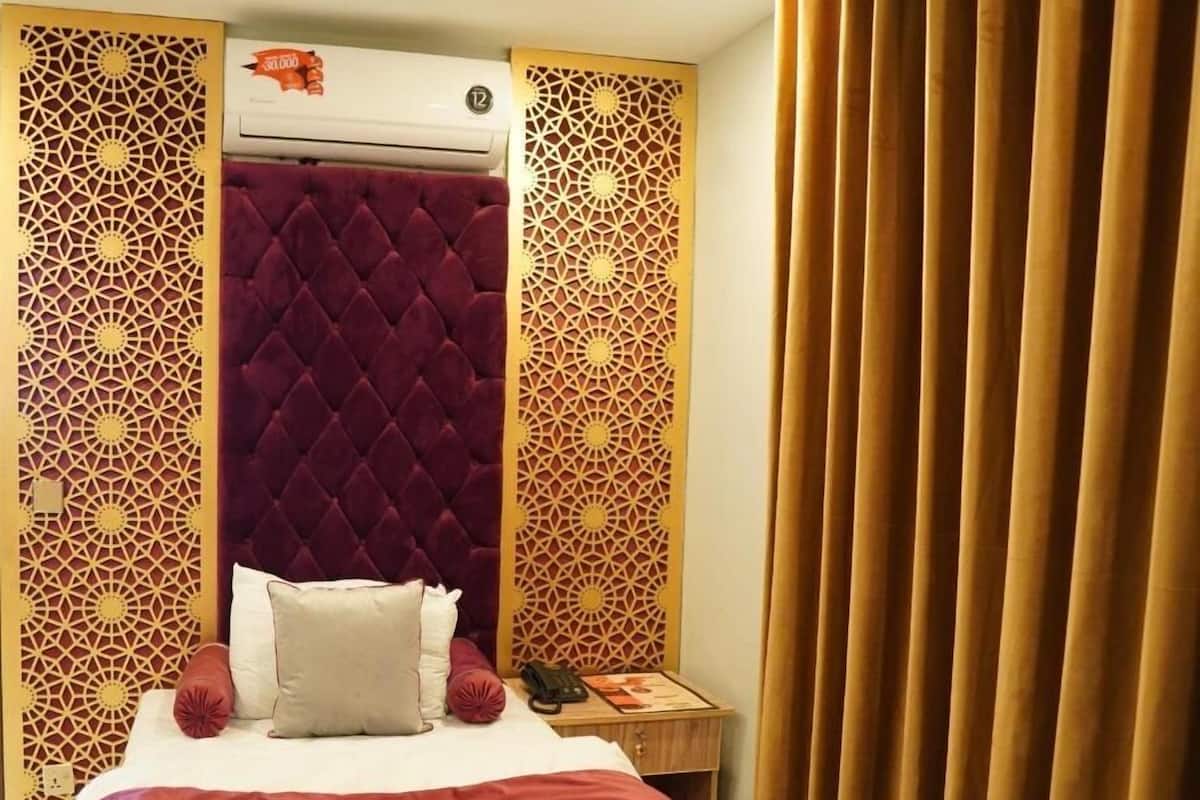 A hotel room with a bed, a red velvet headboard, decorative panels, a bedside table with a phone, and a curtain.