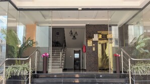 Entrada de hotel con fachada de vidrio, una recepción y una escalera que conduce al interior.