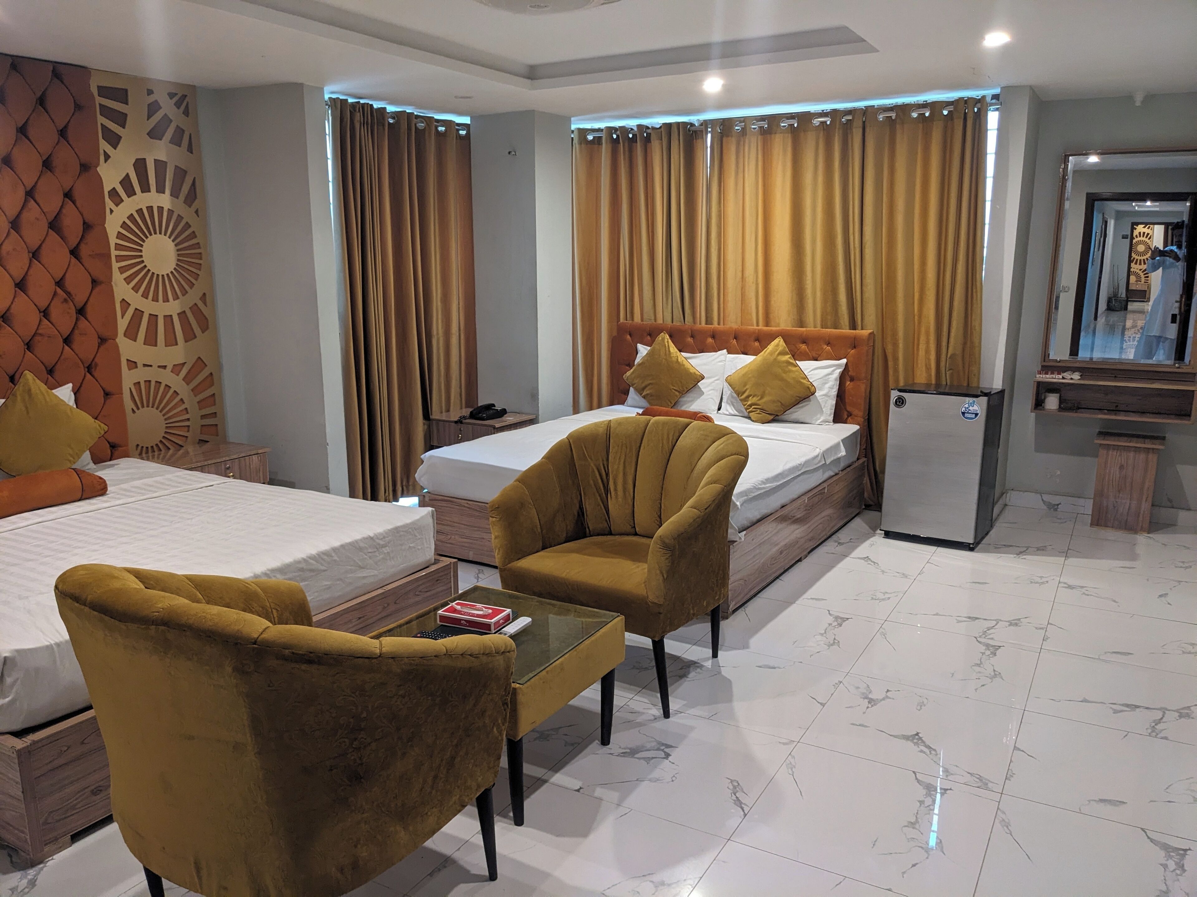 A hotel room with two beds, a sofa, a small table, a refrigerator, and a mirror.
