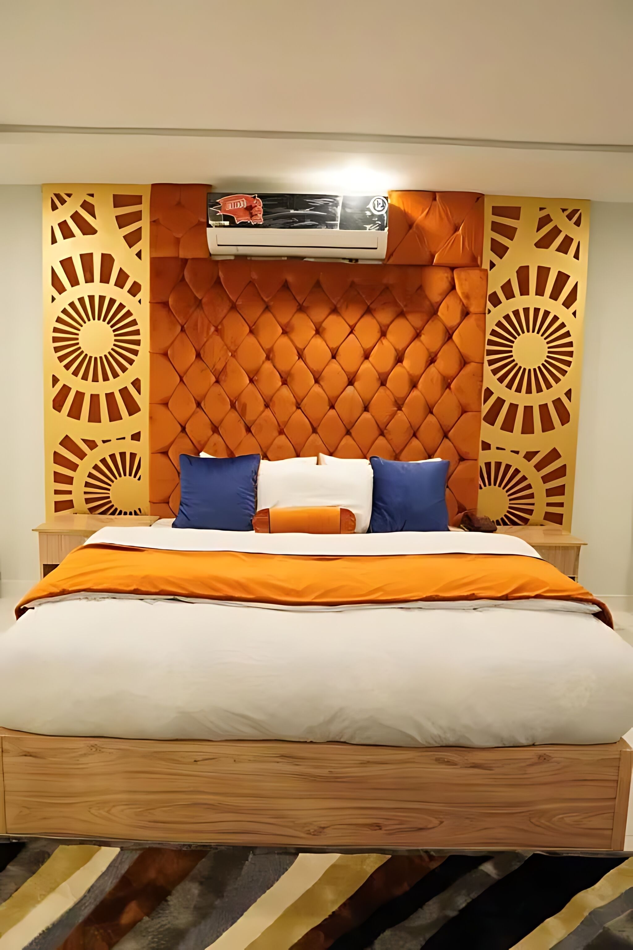 A bed with a wooden frame, a tufted orange headboard, and a patterned wall panel.