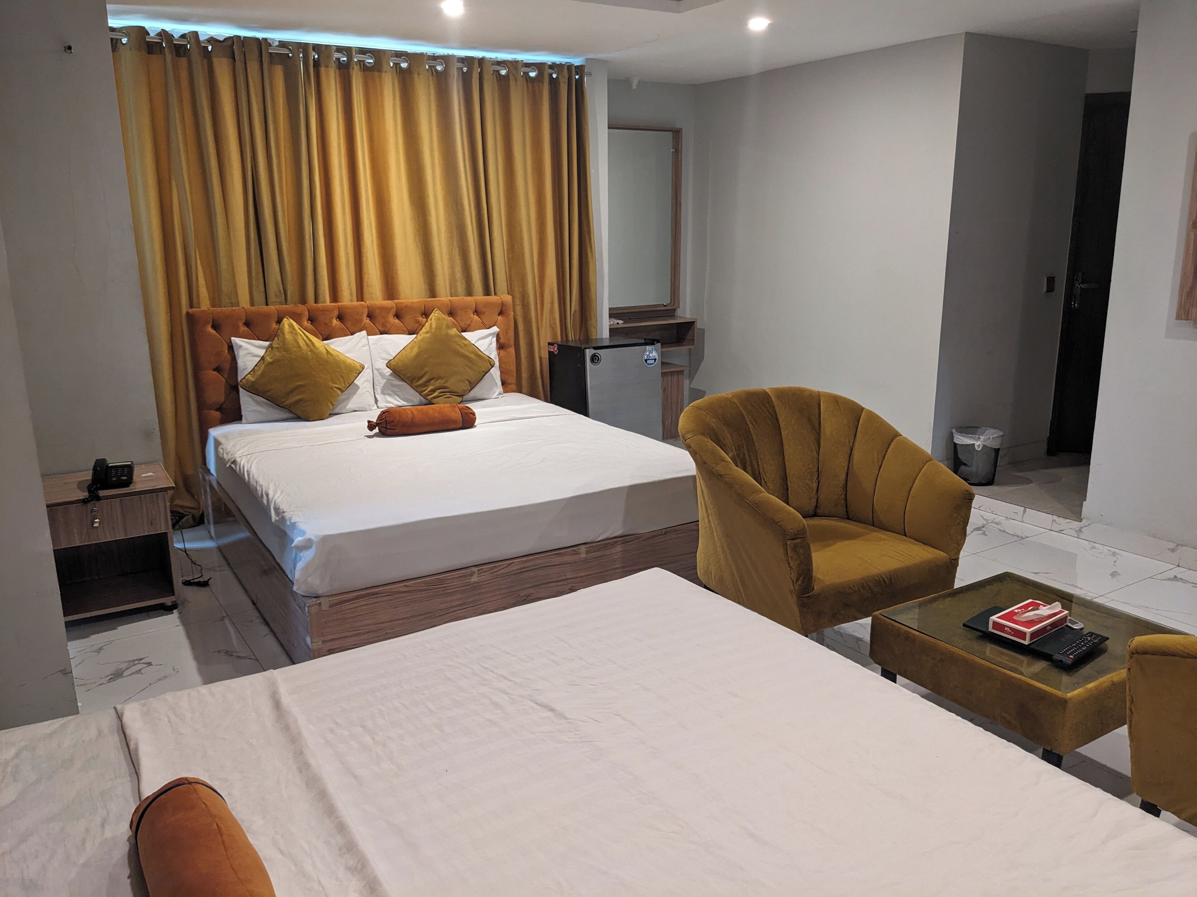 A hotel room with a large bed, a chair, a small table, and a mirror.