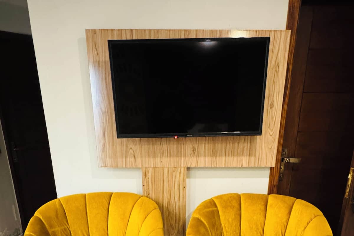 Two yellow armchairs and a small table in a room with a large flat-screen TV mounted on a wooden panel.