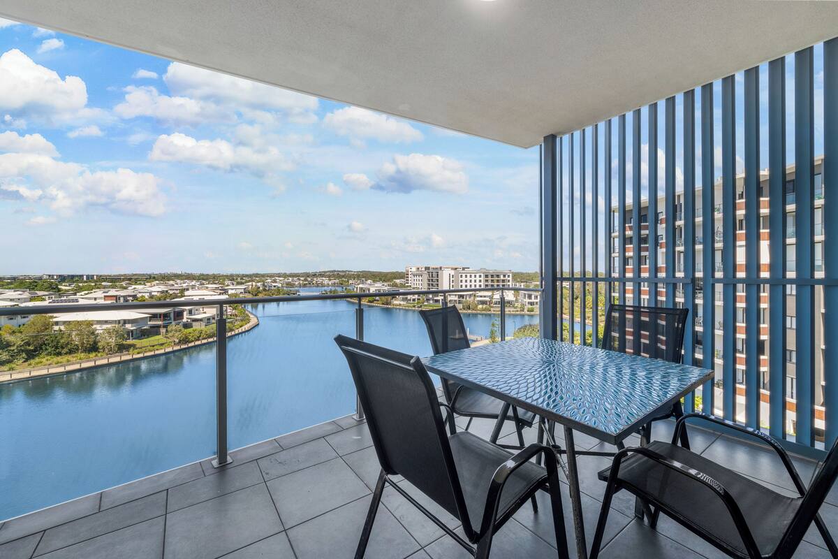A balcony with a table and chairs overlooking a river and cityscape.