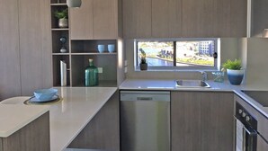 Moderni keittiö, jossa on sisäänrakennettu astianpesukone, ikkuna, josta avautuu näkymä kaupunkimaisemaan, sekä hylly koriste-esineille.