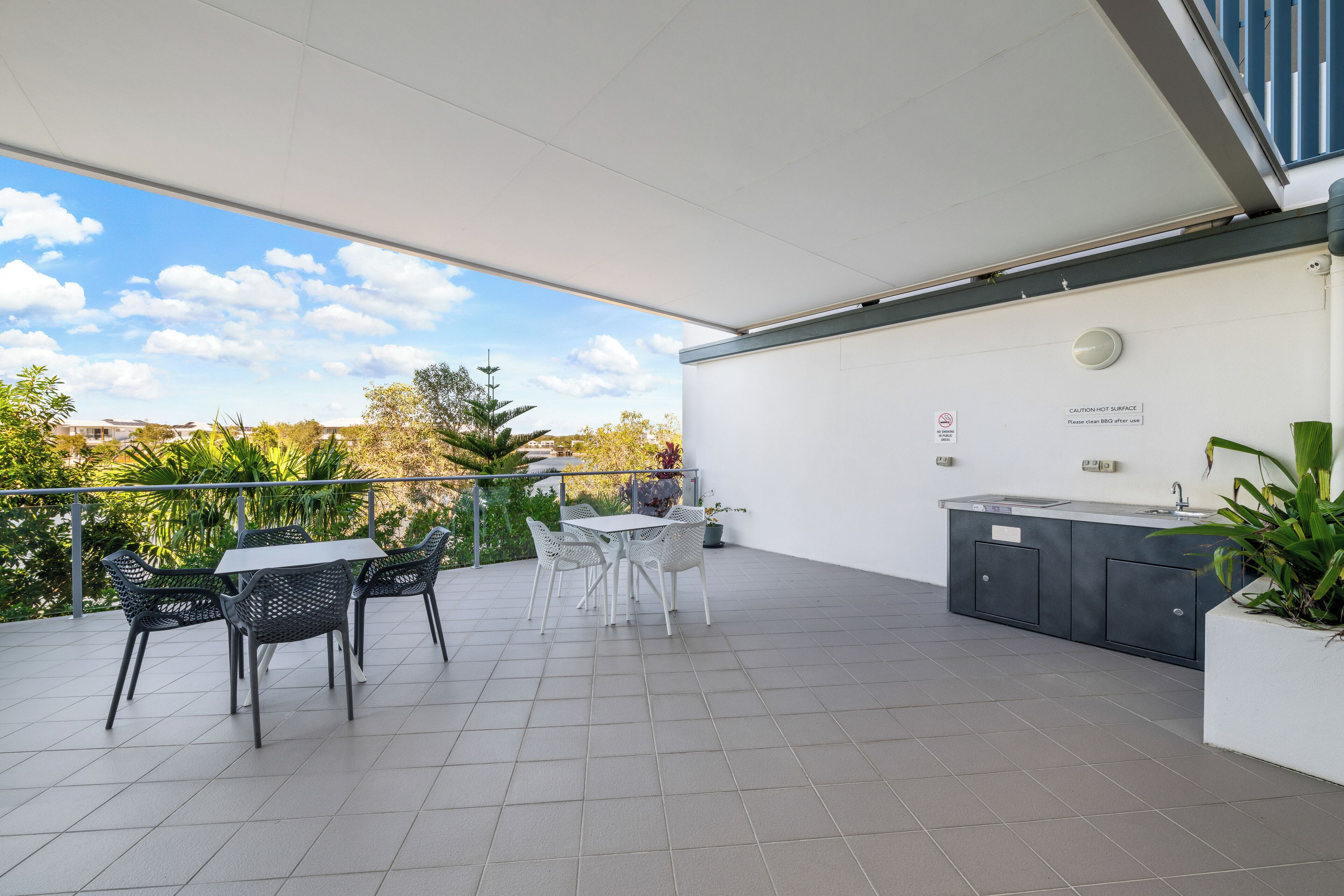 A covered patio with a table and chairs, a built-in kitchen area, and a view of the surrounding greenery.