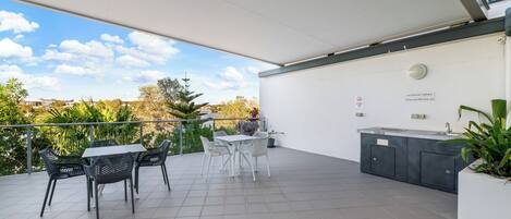 A covered patio with a table and chairs, a built-in kitchen area, and a view of the surrounding greenery.