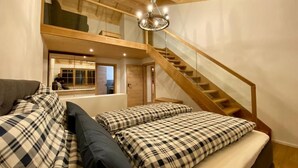 Ein Schlafzimmer im Loft-Stil mit einer Holztreppe, einem Chandelier und einem Sofa mit Karomuster-Bettwäsche.