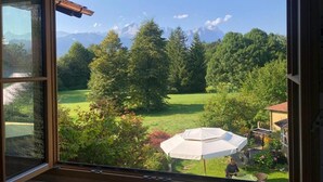 Blick aus einem Fenster mit Holzrahmen auf eine grüne Landschaft mit Bäumen und einem weißen Sonnenschirm.