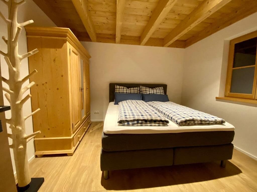 A bedroom with a bed, a wooden wardrobe, and a window.