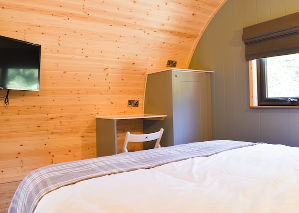 A bedroom with a bed, a desk, a chair, a television mounted on the wall, and a window.
