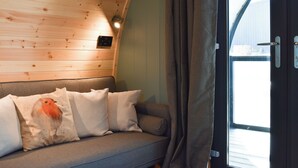 A wooden ceiling, a grey sofa with white cushions, a window with curtains, and a door with a handle. - 1 bedroom accommodation in Wangford, near Southwold (Wangford, near Southwold)
