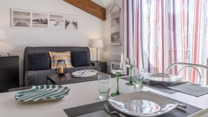 A dining area with a table set for two, a sofa in the background, and a window with striped curtains.