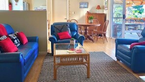 Un salon avec un canapé bleu, une table basse en verre et un coin repas comprenant une table et des chaises en bois.