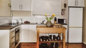 Une cuisine avec des meubles blancs, une table en bois sur laquelle sont posées des casseroles, un four à micro-ondes et un réfrigérateur.