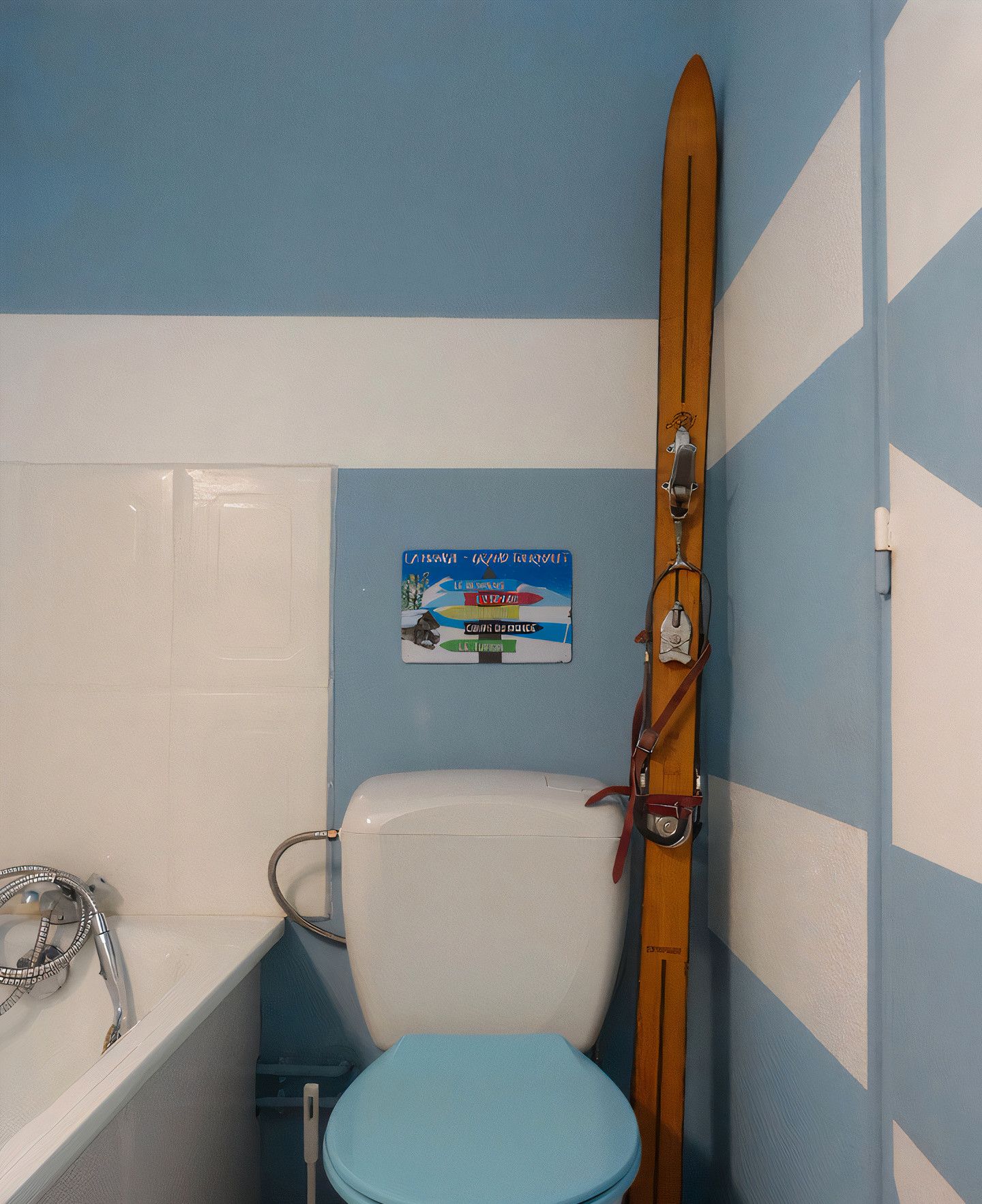 Une salle de bain aux couleurs bleu et blanc, une paire de skis en bois appuyée contre le mur et un panneau avec du texte.