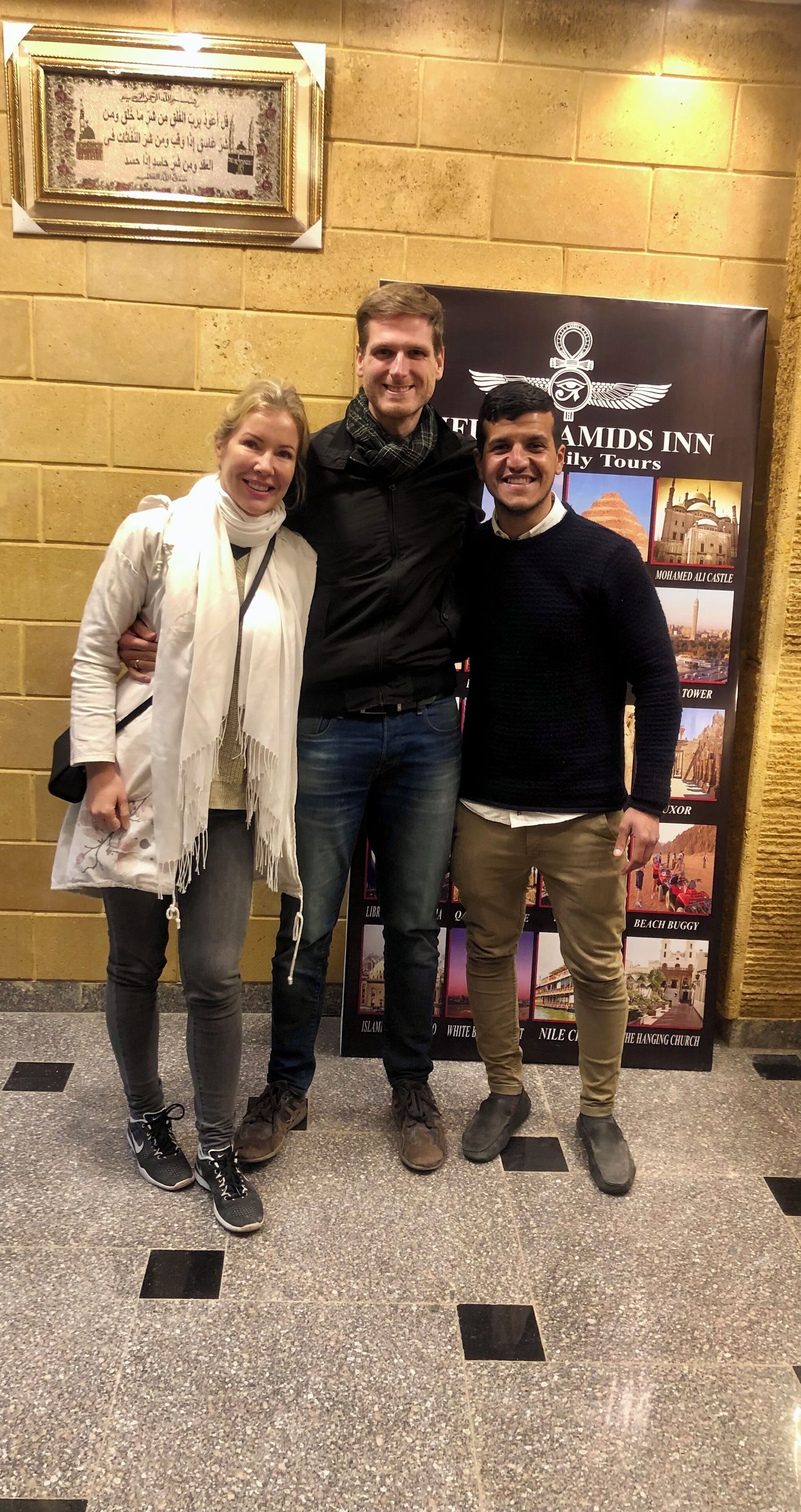 Tres personas de pie frente a una pared con una placa enmarcada y un cartel que anuncia recorridos.