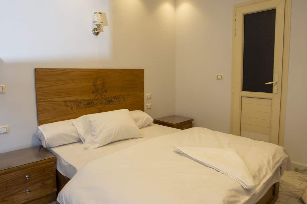 Siististi pedattu sänky hotellihuoneessa, jossa on puinen pääty, yöpöytä ja kuviollinen matto lattialla.