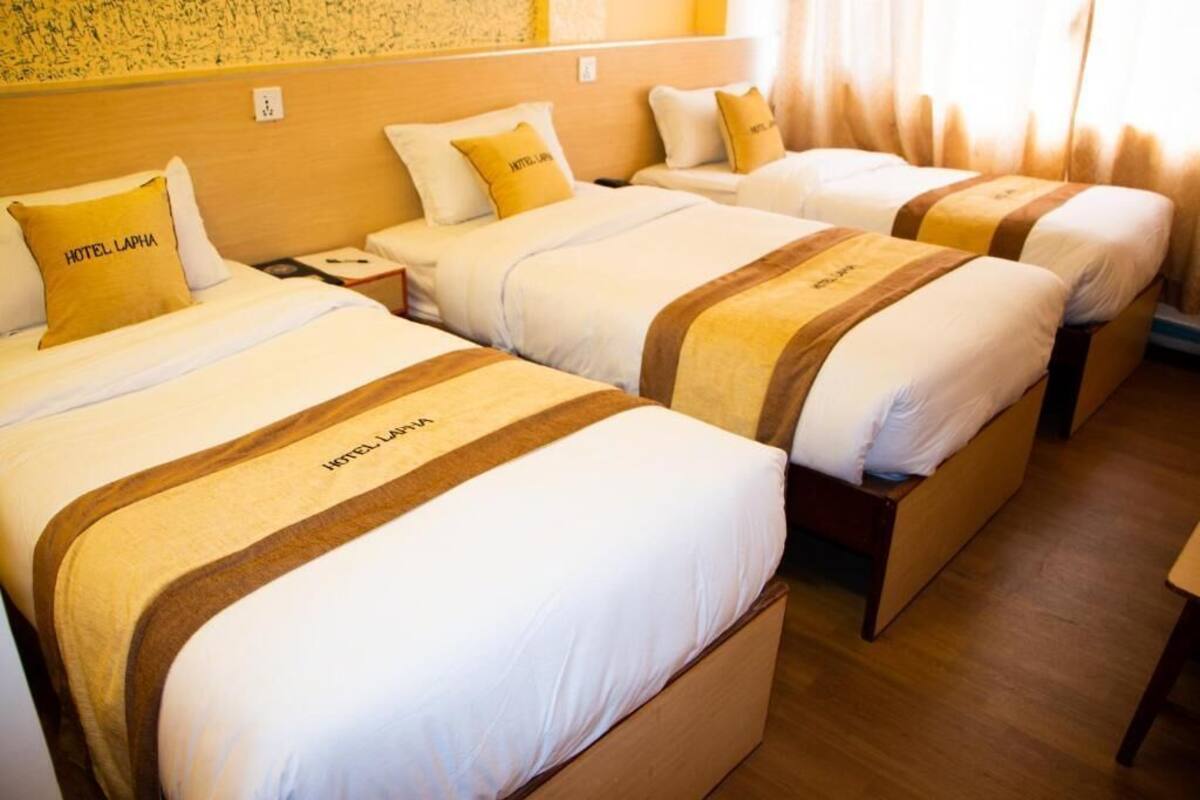 A hotel room with three beds, each with a headboard and pillows labeled "HOTEL LAPHA."
