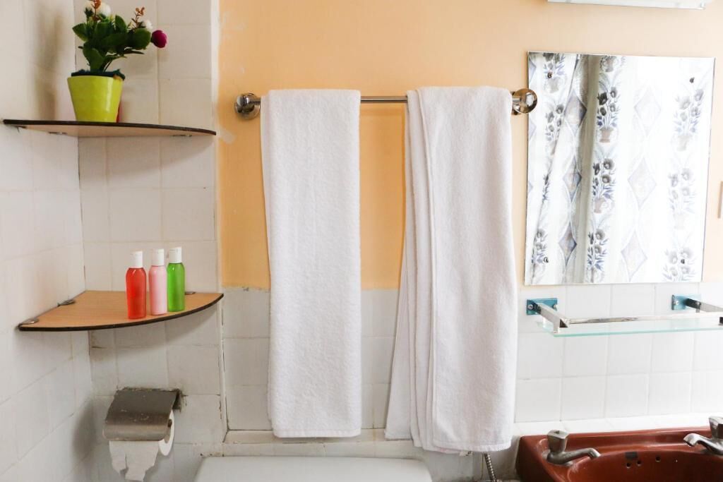 Ein Badezimmer mit einer weißen Badewanne, einer Glasablage für Toilettenartikel und einem Spiegel mit floralem Muster.