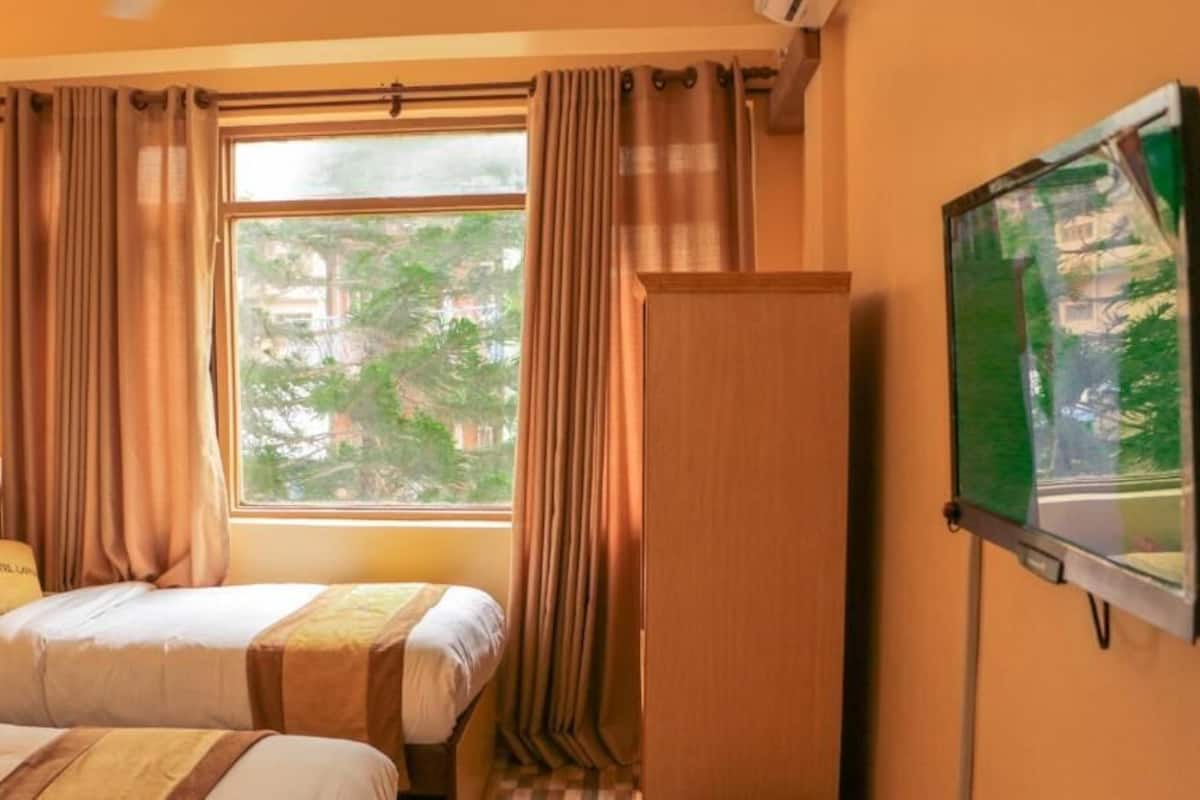 A hotel room with a bed, a desk, a chair, a TV, and a window with curtains.