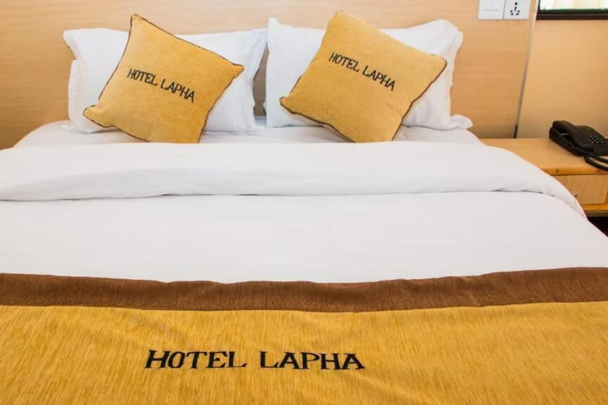A hotel bed with two pillows labeled "HOTEL LAPHA" and a bedspread with the same text.