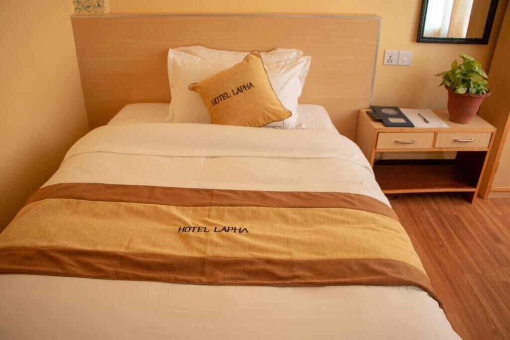 A hotel room with a bed, a nightstand, a potted plant, and a mirror on the wall.