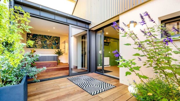 Uma casa moderna com um deck de madeira, um tapete preto e branco e diversas plantas.