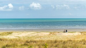 Uma praia com duas pessoas sentadas em uma duna, com vista para o oceano.