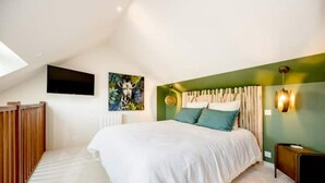 Um quarto com uma cama grande, uma parede verde de destaque, uma TV montada e uma pintura de uma girafa.