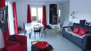 A living room with a sofa, a dining table with chairs, a red bowl on a table, and a television. - House in the Cevennes (Chamborigaud)