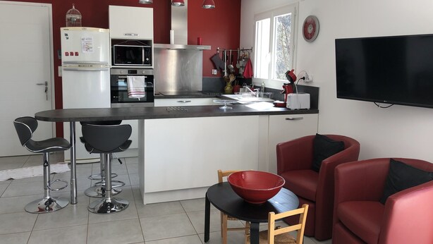 A modern kitchen with a central island, bar stools, a red bowl on a table, and a flat-screen TV mounted on the wall. - House in the Cevennes (Chamborigaud)