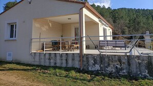 A two-story house with a balcony, a patio area, and a view of a forested hill. - House in the Cevennes (Chamborigaud)