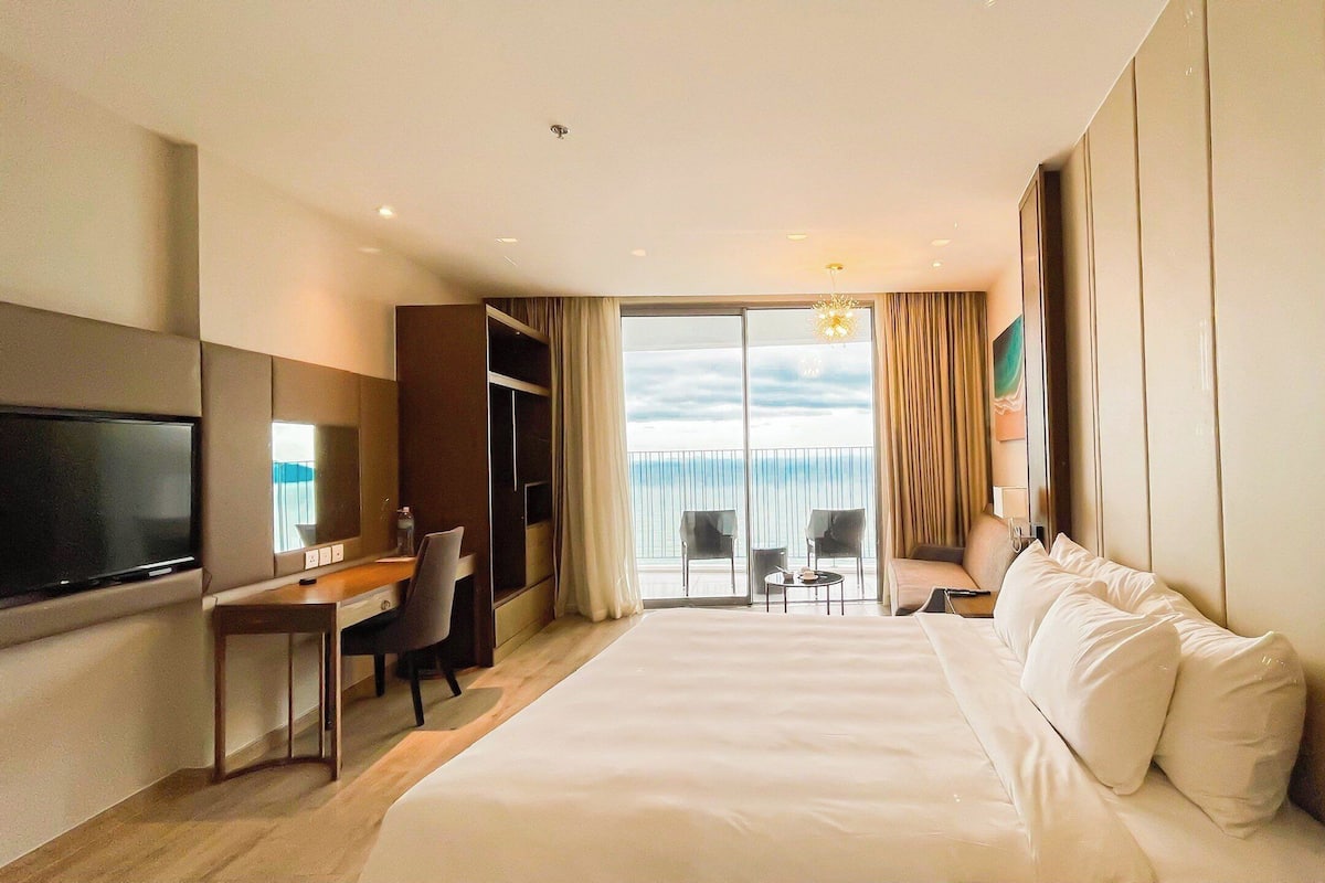 Habitación de hotel con una cama grande, escritorio, televisor y balcón con vistas al océano.